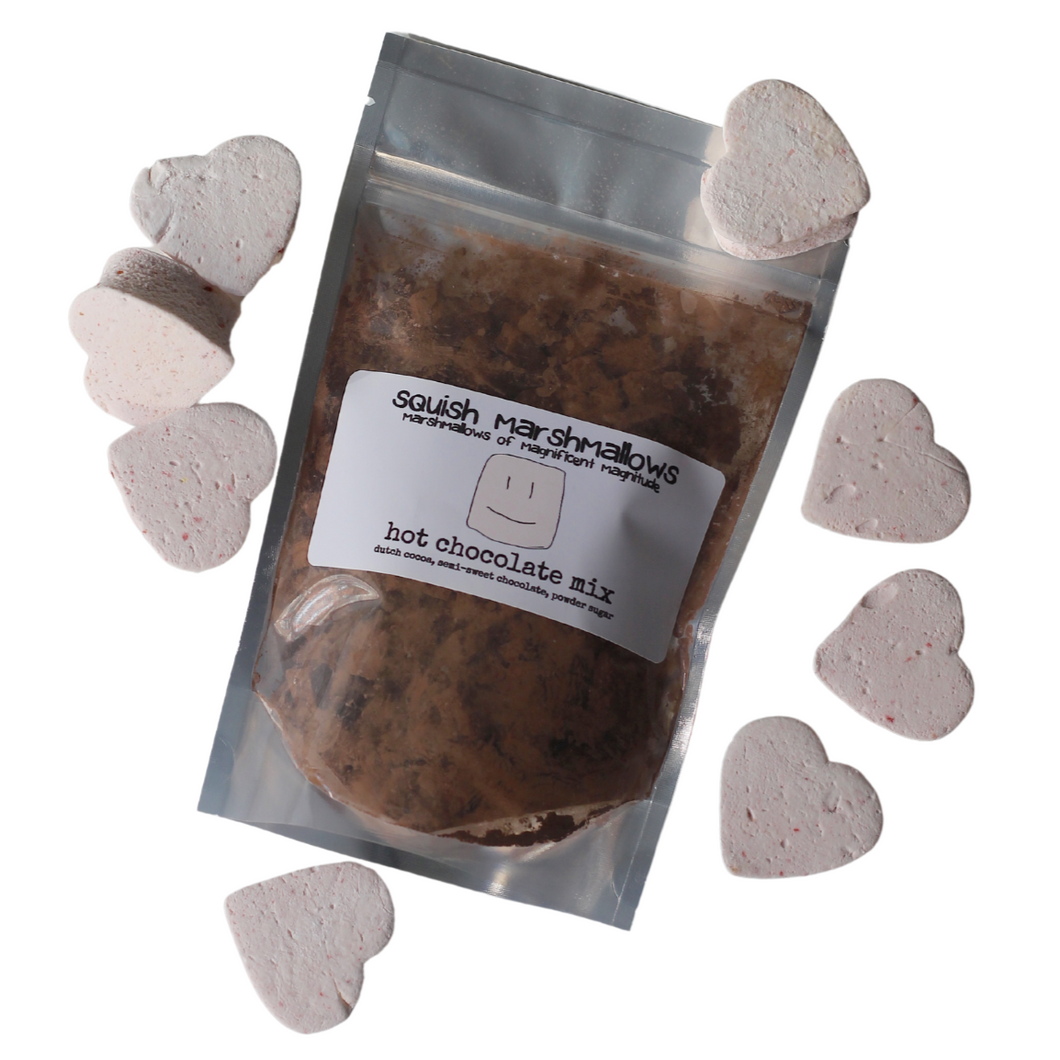Pack of hot chocolate mix, containing chocolate chunks, cocoa powder and sugar, with strawberry pink marshmallow hearts surrounding it