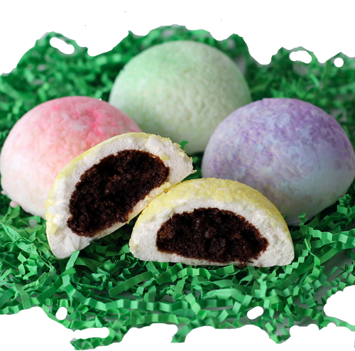 cottontails, 4 dome shaped marshmallows coated with shredded coconut, with chocolate cake stuffed inside. cottontails have colored coating in yellow, pink, purple and green, sitting on a bed of green shredded crinkle paper