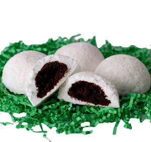 cottontails, 4 dome shaped marshmallows coated with shredded coconut, with chocolate cake stuffed inside. cottontails are white, sitting on a bed of green shredded crinkle paper